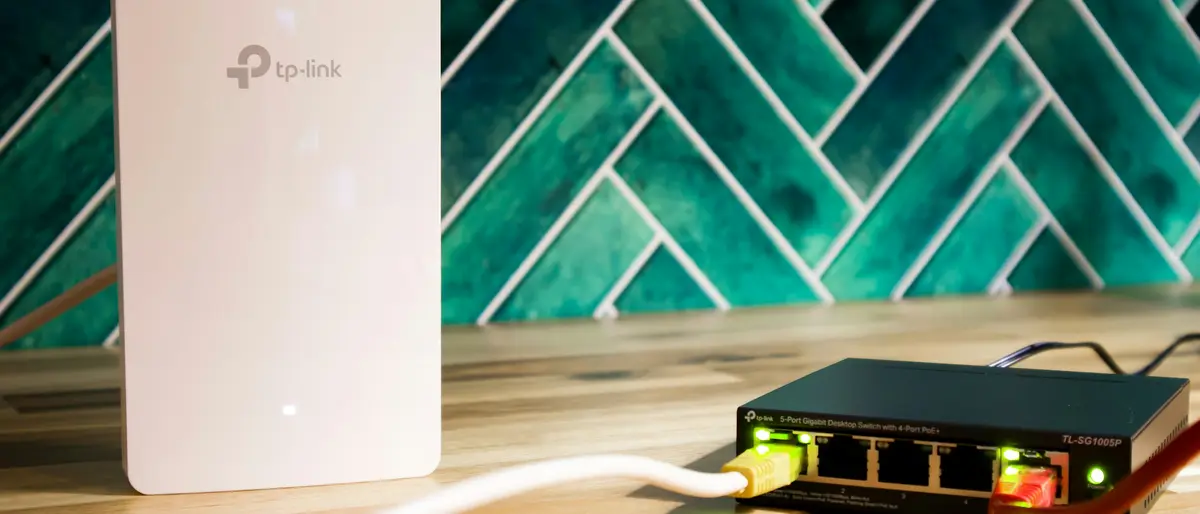 Wit TP-Link-accesspoint naast een kleine PoE-switch met netwerkkabels