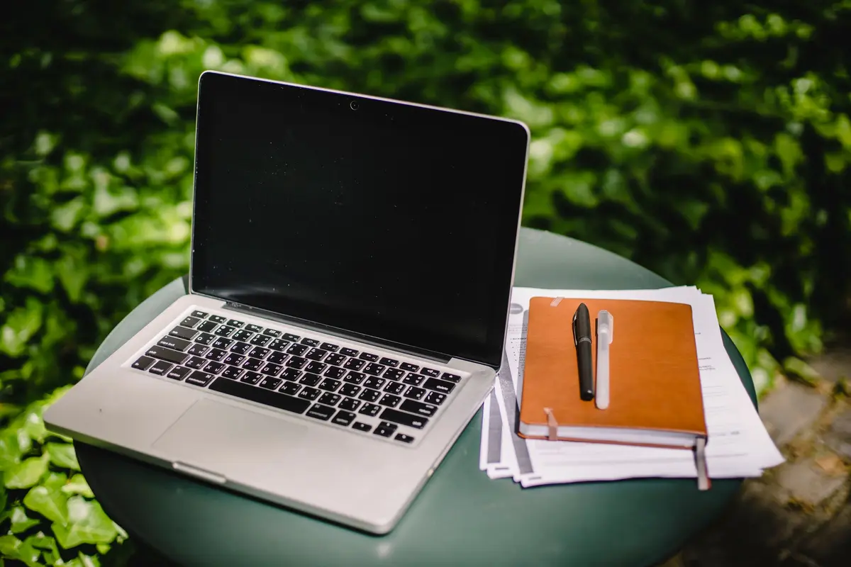Laptop en notitieboek op een tuintafel tussen het groen